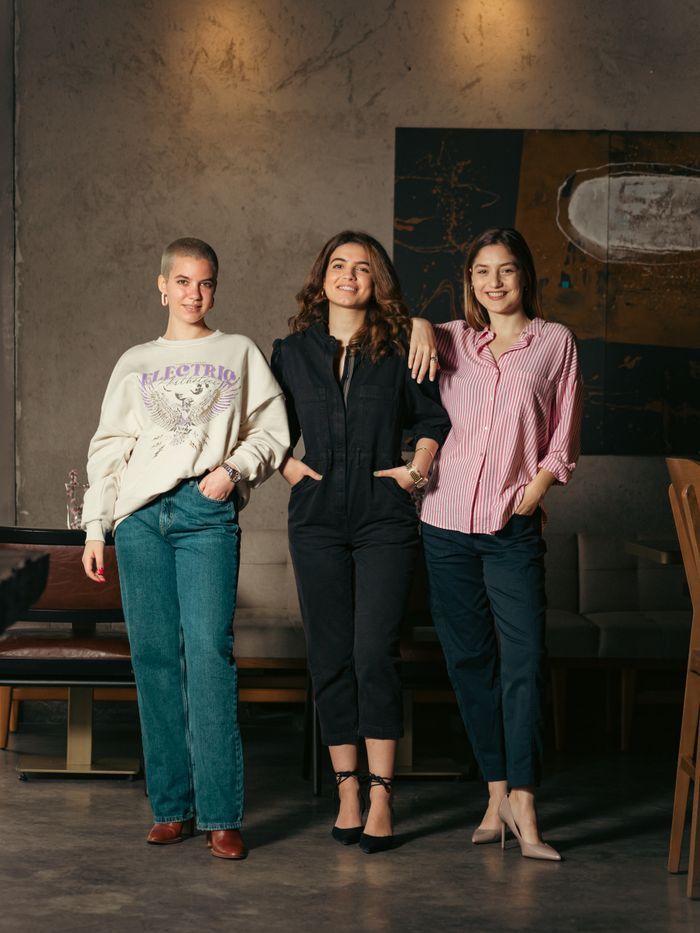 digital Three women casually posing in a stylish indoor setting, showcasing confidence and friendship.
